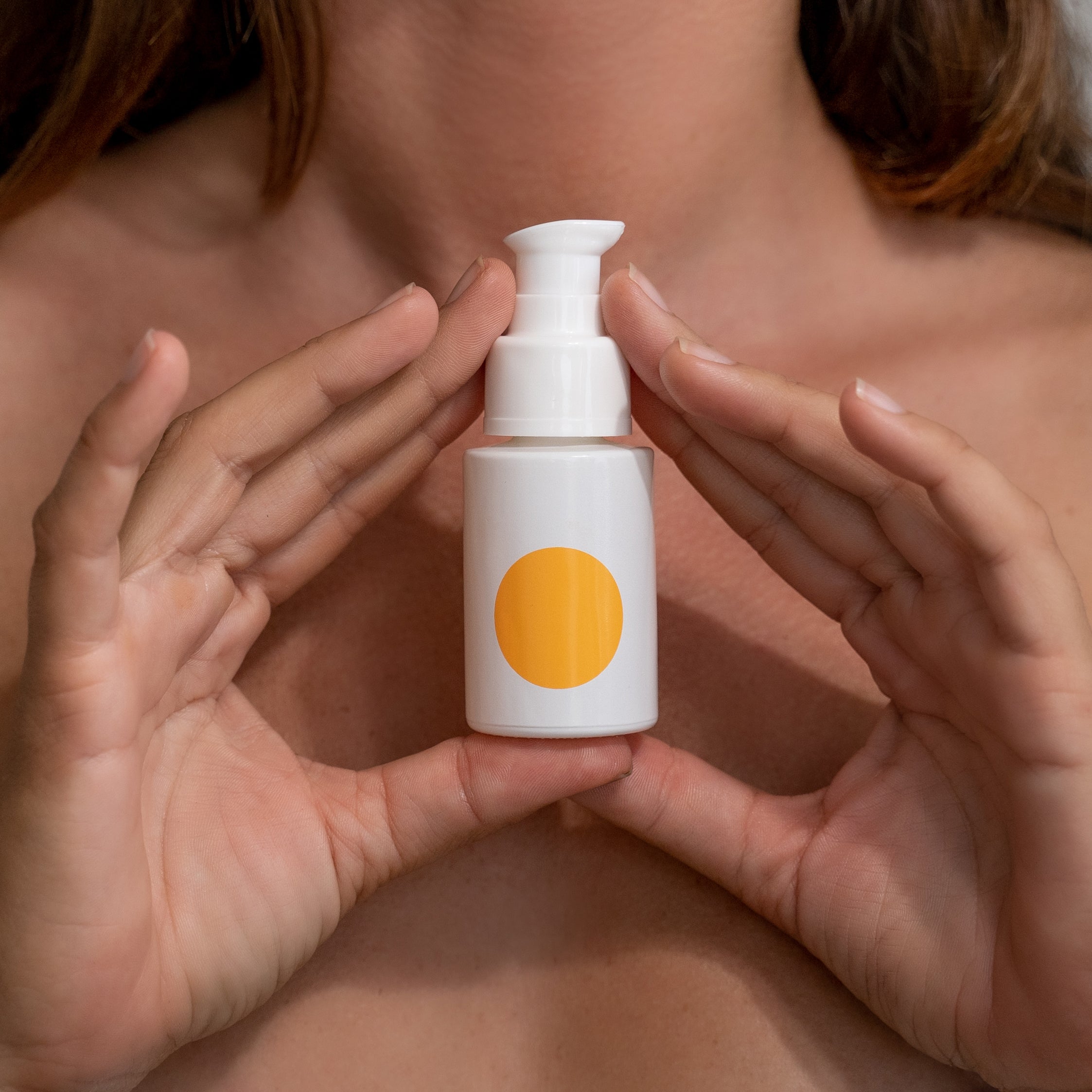 Woman holding Somme Institute Serum bottle with orange dot at neck and décolletage area demonstrating skincare application