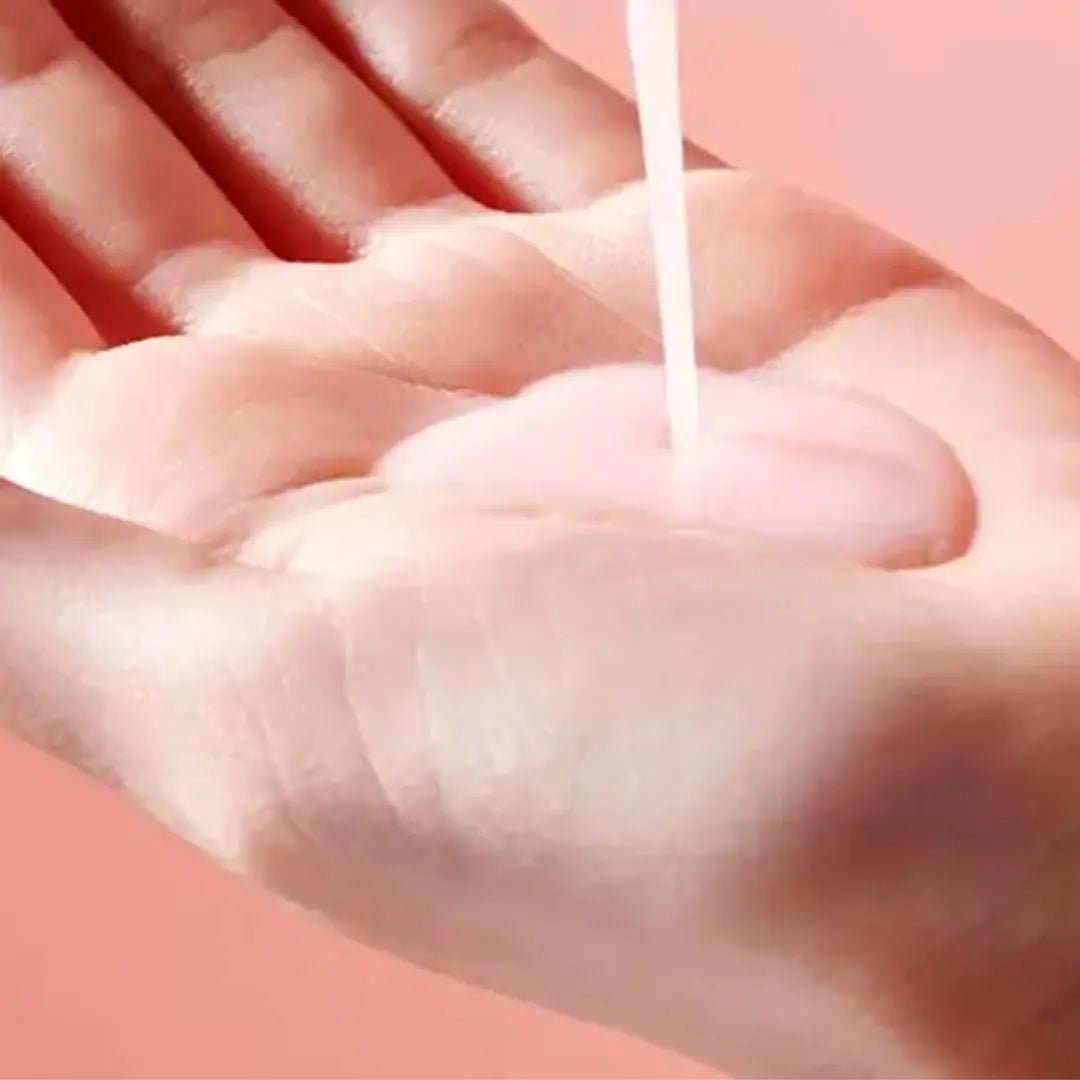 Hand receiving a drop of white liquid on a pink background
